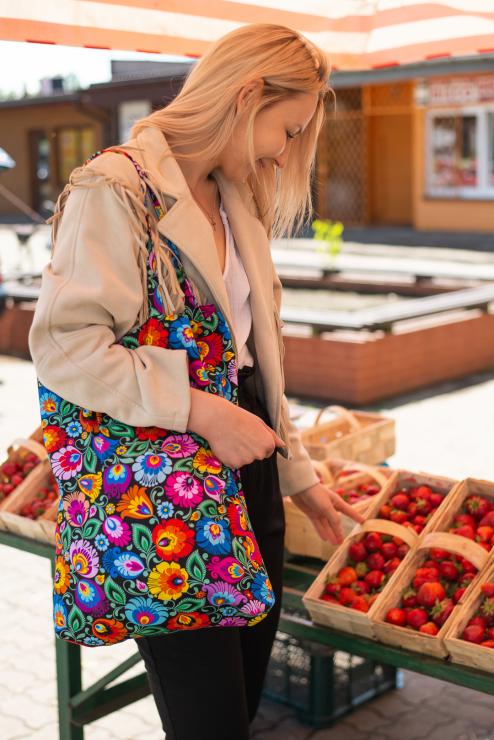 woman picks strawberries while wearing a black folk floral bag